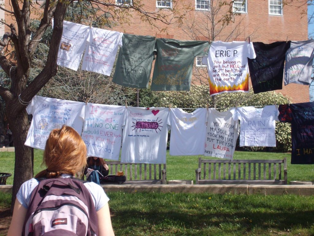 Shirts hung on a clothesline at the University of Maryland. The shirts bear writing intended to support victims of sexual assault, but some of them are angry and some accusatory. One shirt lists the name of a student and says "you belong in jail but hell will be second best. You are the scum of the earth."