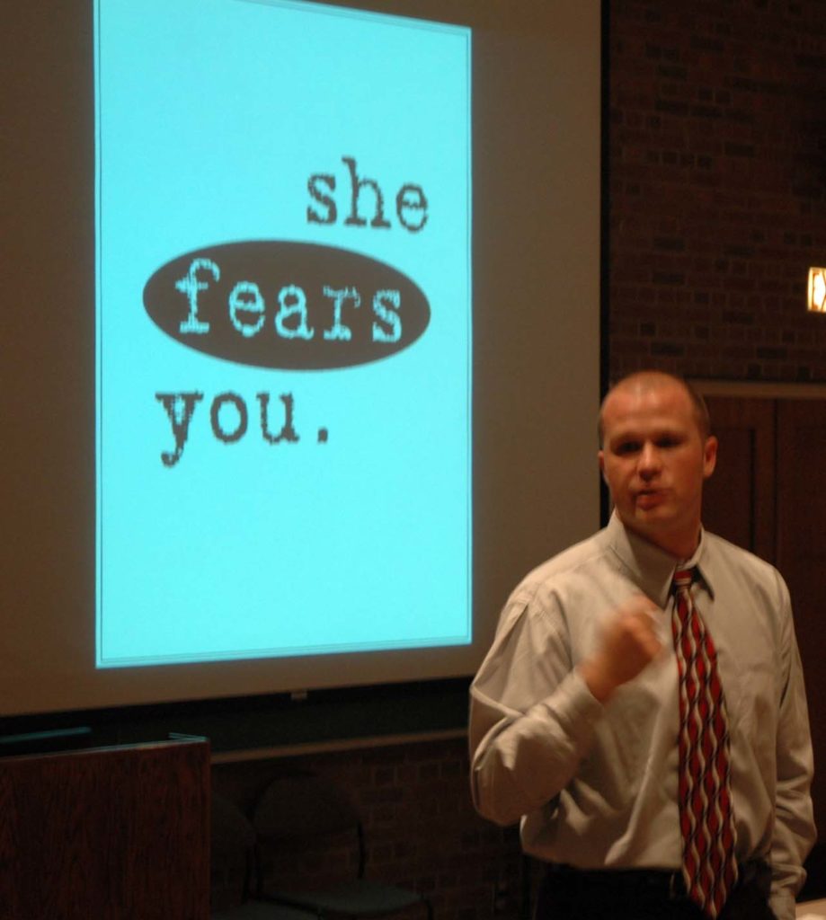 Keith Edwards giving his "She Fears You" presentation to first-year students. In the background is a screen that says "She Fears You" in large letters.