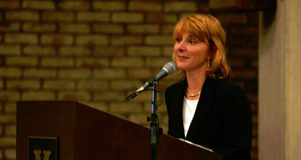 A still image of Beth Fortune speaking before an audience. She appears confident, if not haughtily so.