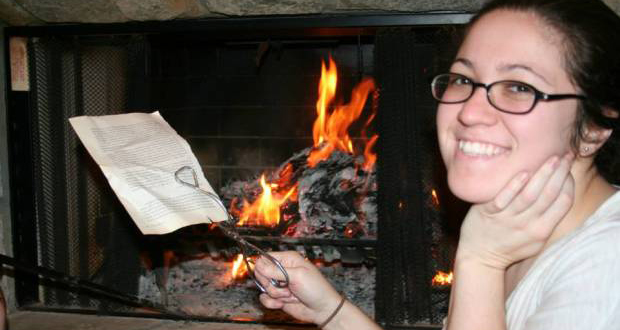 A photo of a woman burning pages of the book The War Against Boys by Christina Hoff-Sommers. The woman appears happy as she puts pages in the fire.